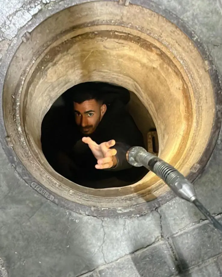 לידור בתוך שוחת ביוב, מושיט יד לכבל של מצלמת הצנרת