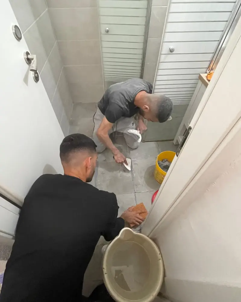 לידור ועובד נוסף בעבודה בחדר רחצה, כורעים ליד הריצוף
